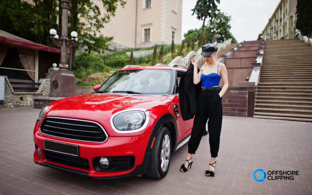 Wide shot of a red car highlighting its full front view, background scenery, and a model positioned beside it.