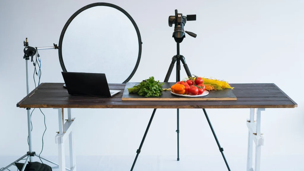 Food product photography setup with vegetables, reflector, and camera on tripod