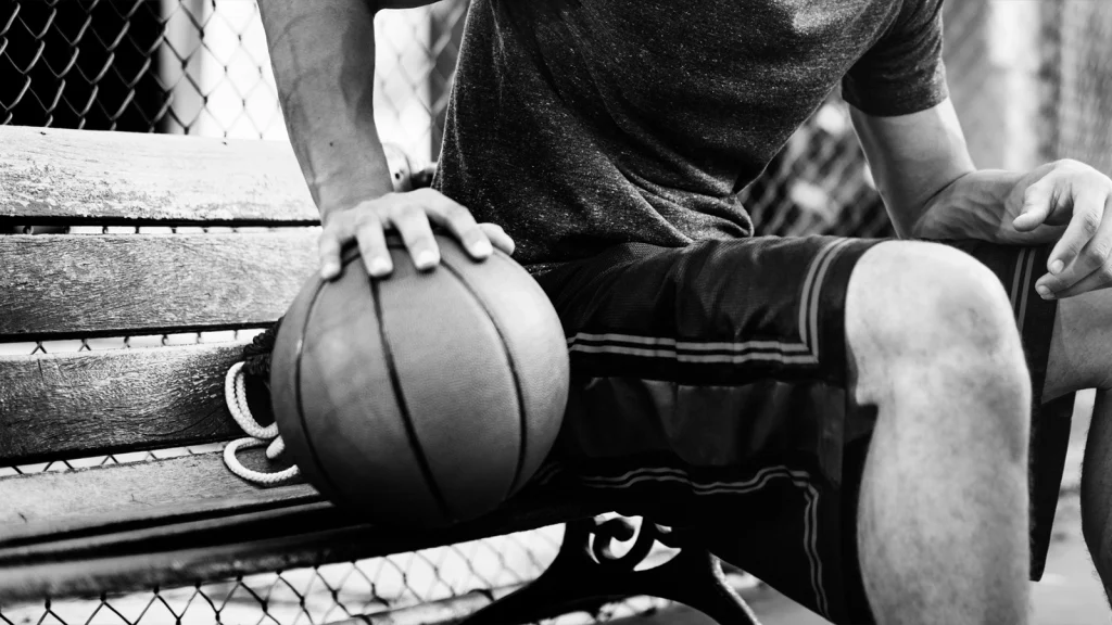 Black and white close-up of a basketball player resting on a bench, reflecting the classic style of early sports photography