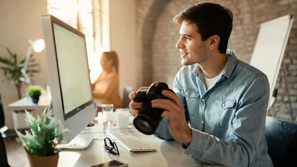 Professional photo editor reviewing photographs on a computer beside a digital camera