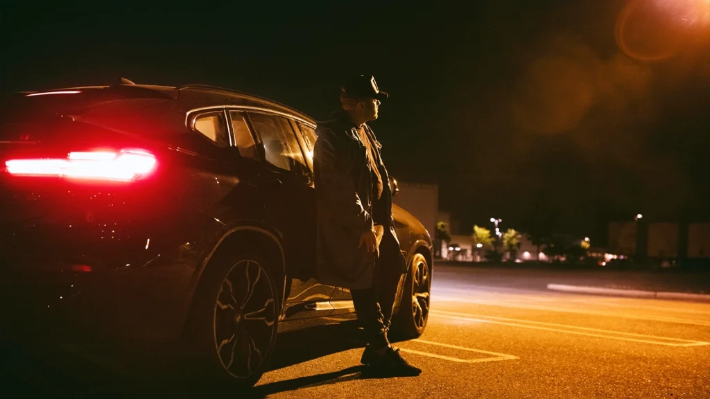 Car parked under streetlights at night with a person creating a dramatic automotive photography composition.