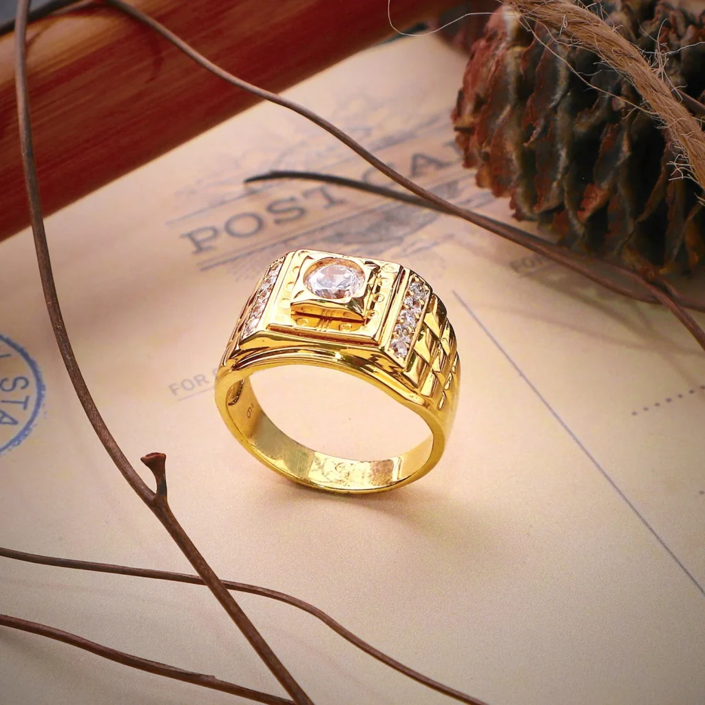 A gold ring with clear gemstones rests on a vintage postcard beside twigs and a pine cone.