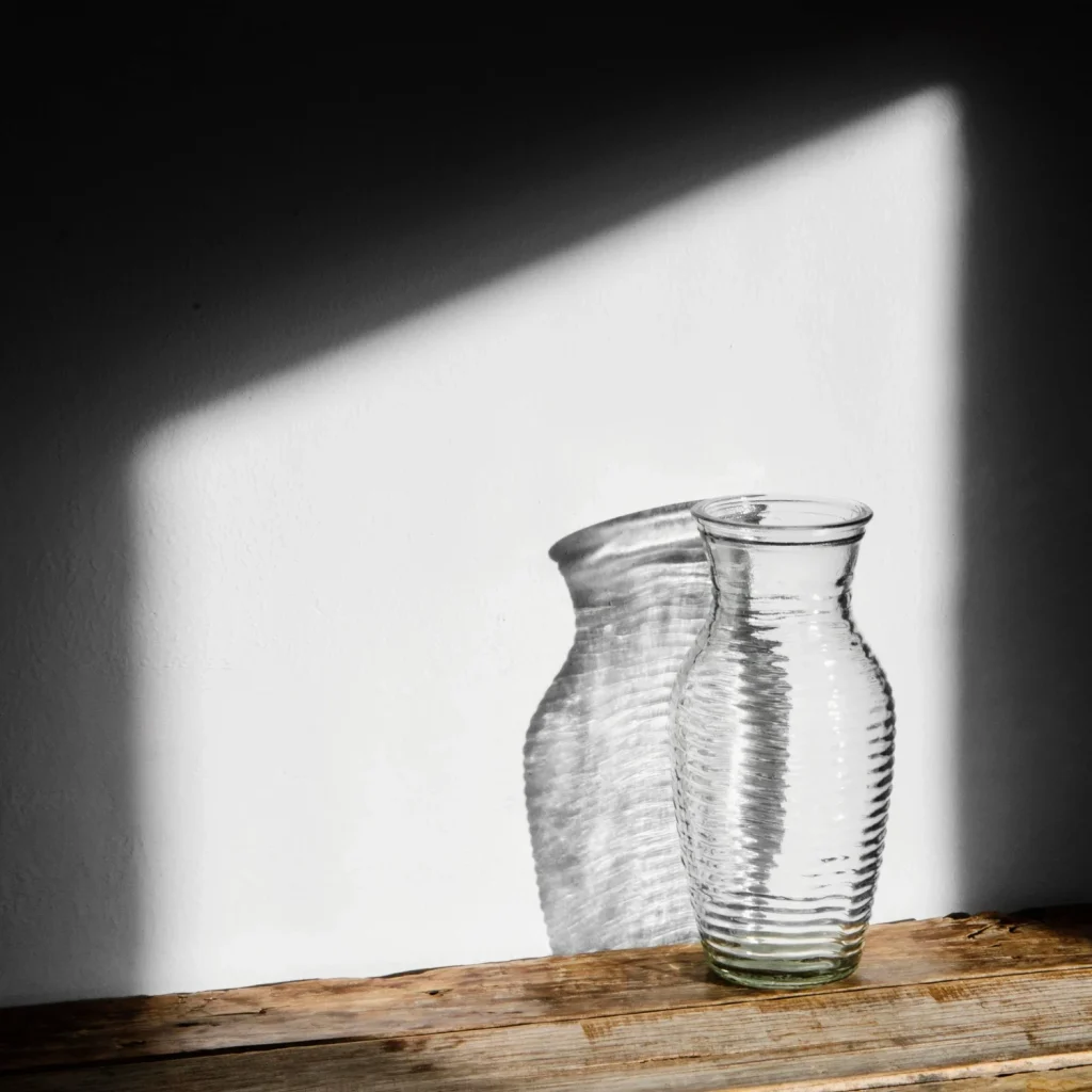 Minimalist glass vase with natural sunlight creating clean shadows on a white wall.