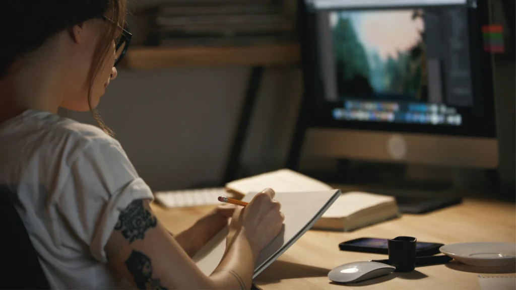 Designer sketching brand style notes beside an editing screen for outsourced brand consistency