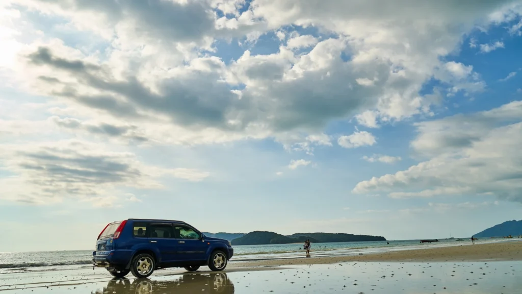 Blue SUV photographed on a beach with coastal scenery