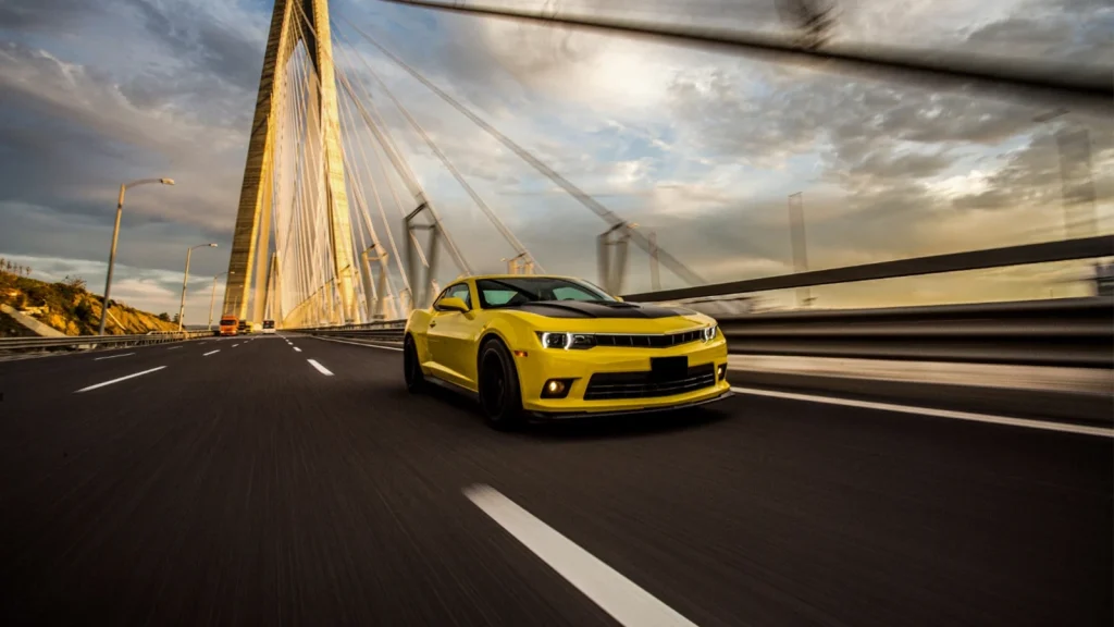 Yellow sports car photographed driving across a large bridge at sunset
