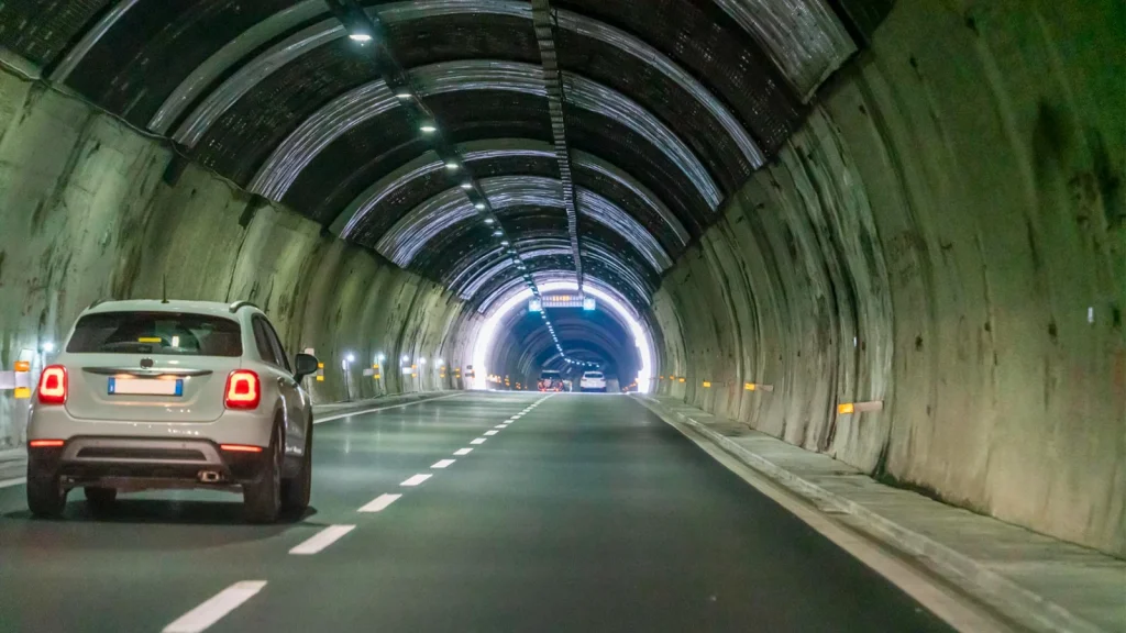 White car photographed inside a tunnel with repeating lights and road lines