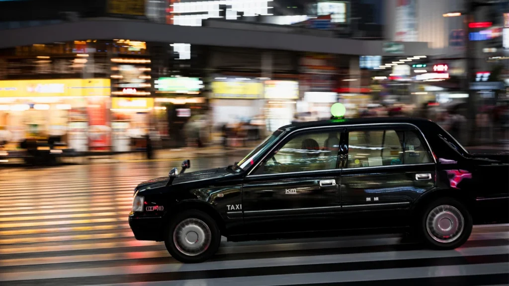 Black car photographed on a busy city street at night with motion blur