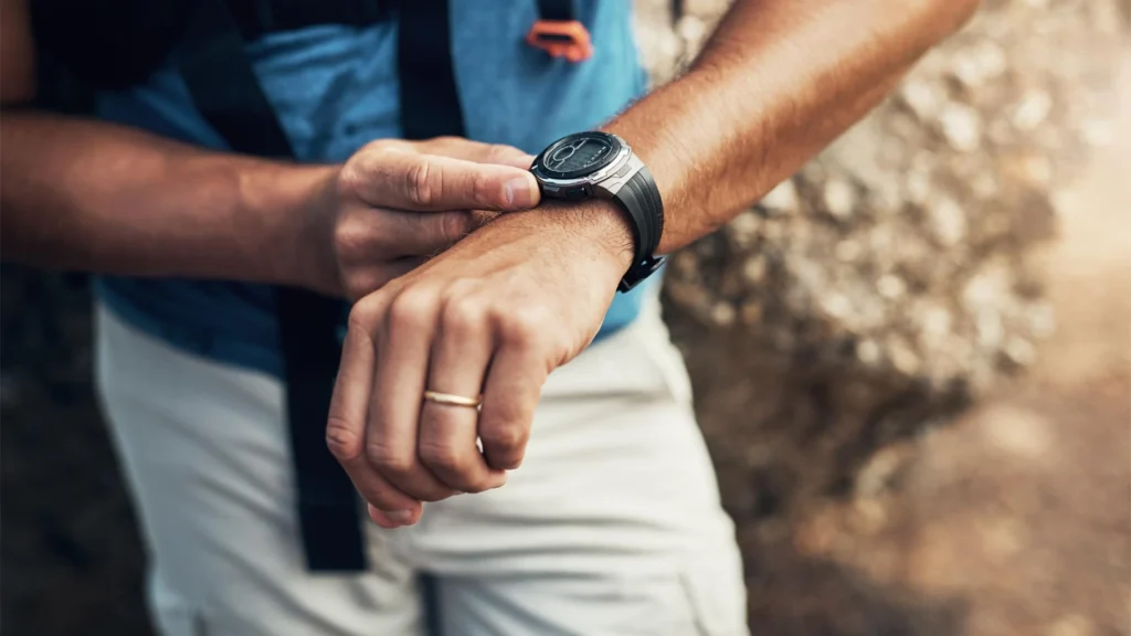 Hiker checking a black outdoor watch on the wrist against a rocky natural backdrop