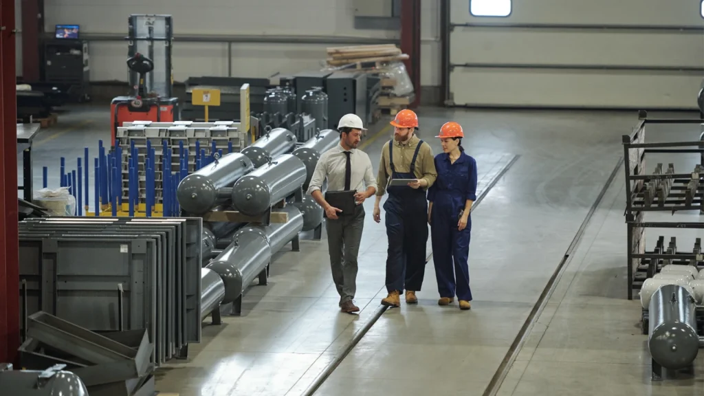 Factory workers and industrial professionals walking through a manufacturing facility with heavy equipment