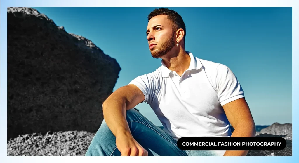 Male model in a white polo and light jeans sitting on rocks against a blue sky, commercial fashion photography
