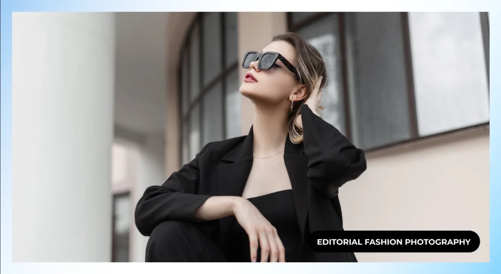 Model in a black blazer and square sunglasses looking upward with a hand in her hair near arched windows, editorial fashion photography